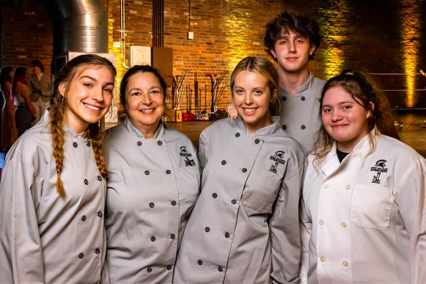 Five students dressed in culinary uniforms smile